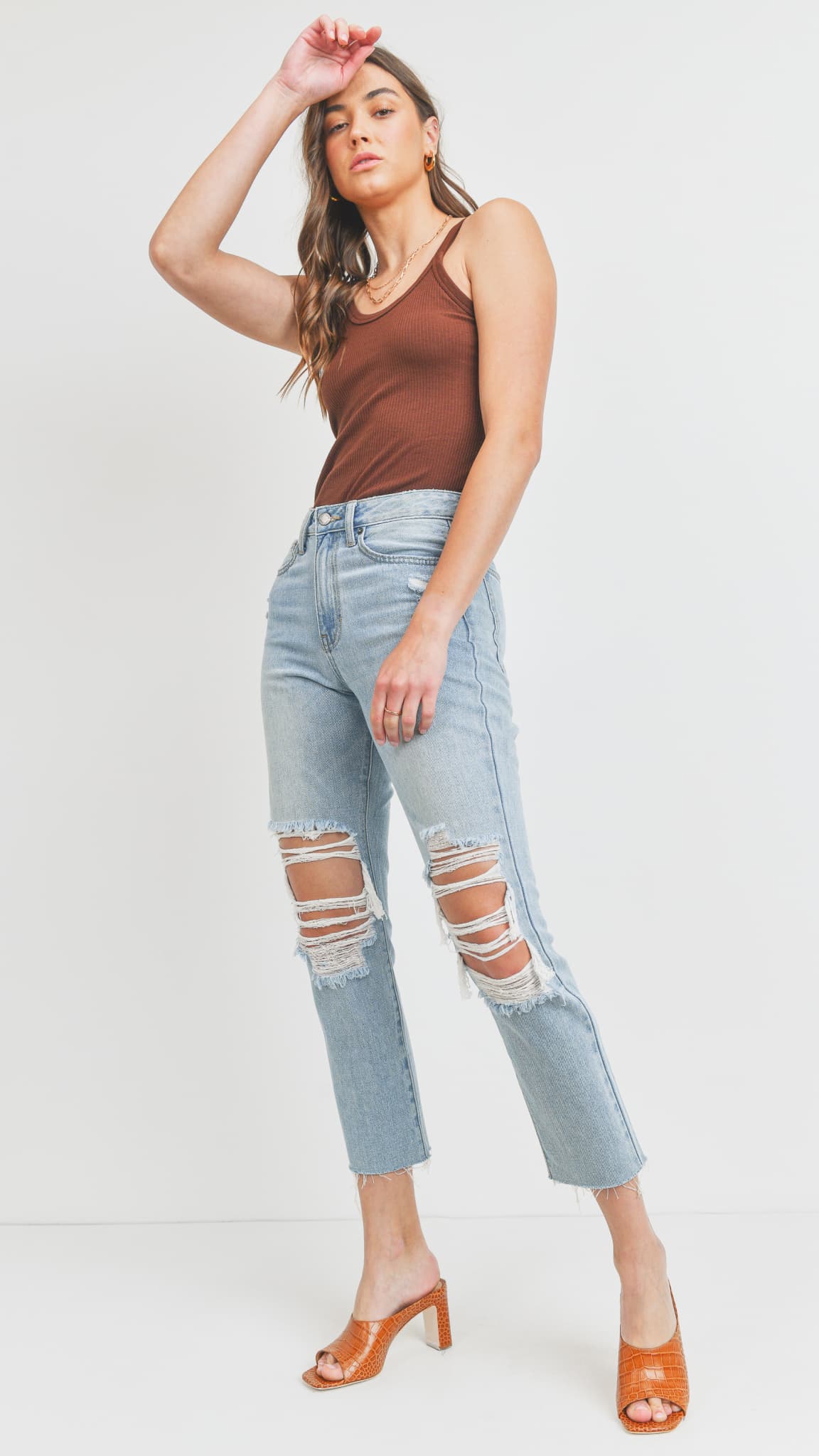 Woman wearing light-wash distressed straight-leg jeans, a brown tank top, and heeled mules