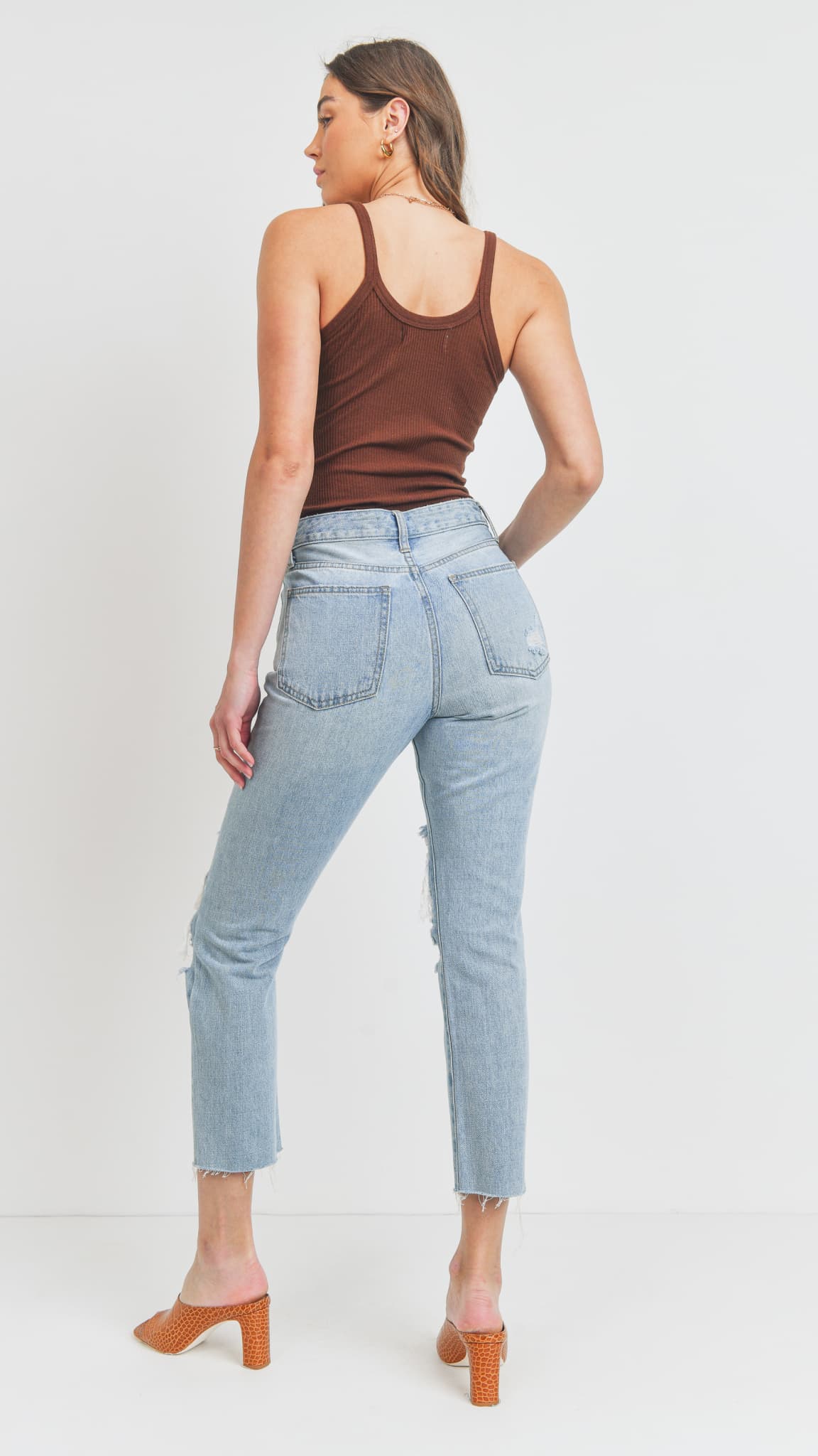 Woman facing backwards, wearing light-wash straight-leg jeans, a brown tank top, and heeled mules
