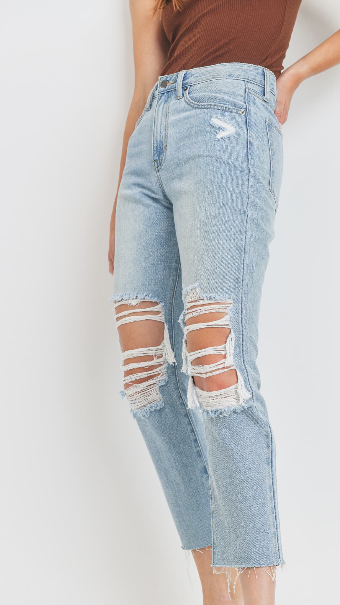 Close-up of light-wash distressed straight-leg jeans and a brown top