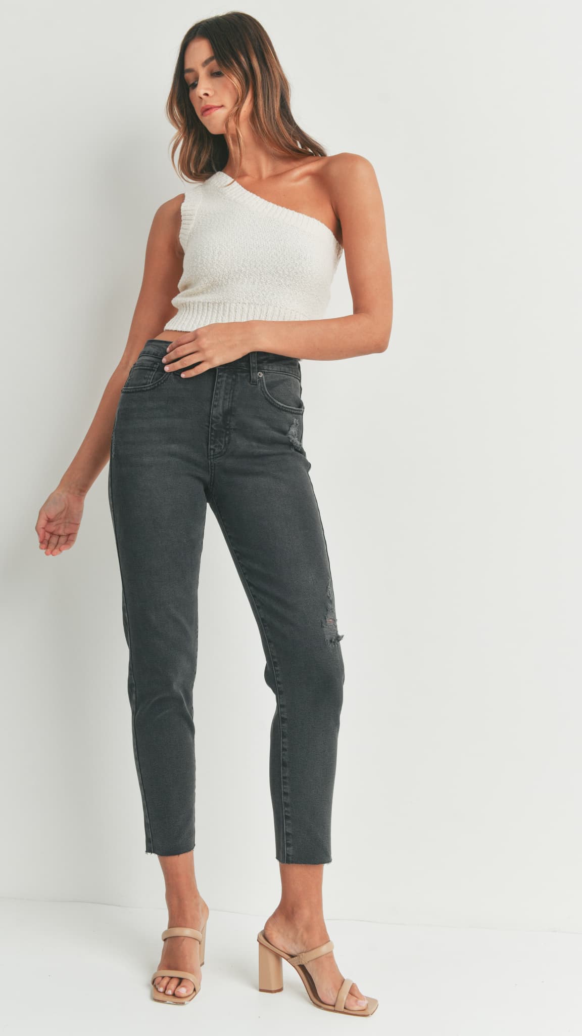 Woman in black skinny jeans, a white knit crop top paired, and beige heeled sandals