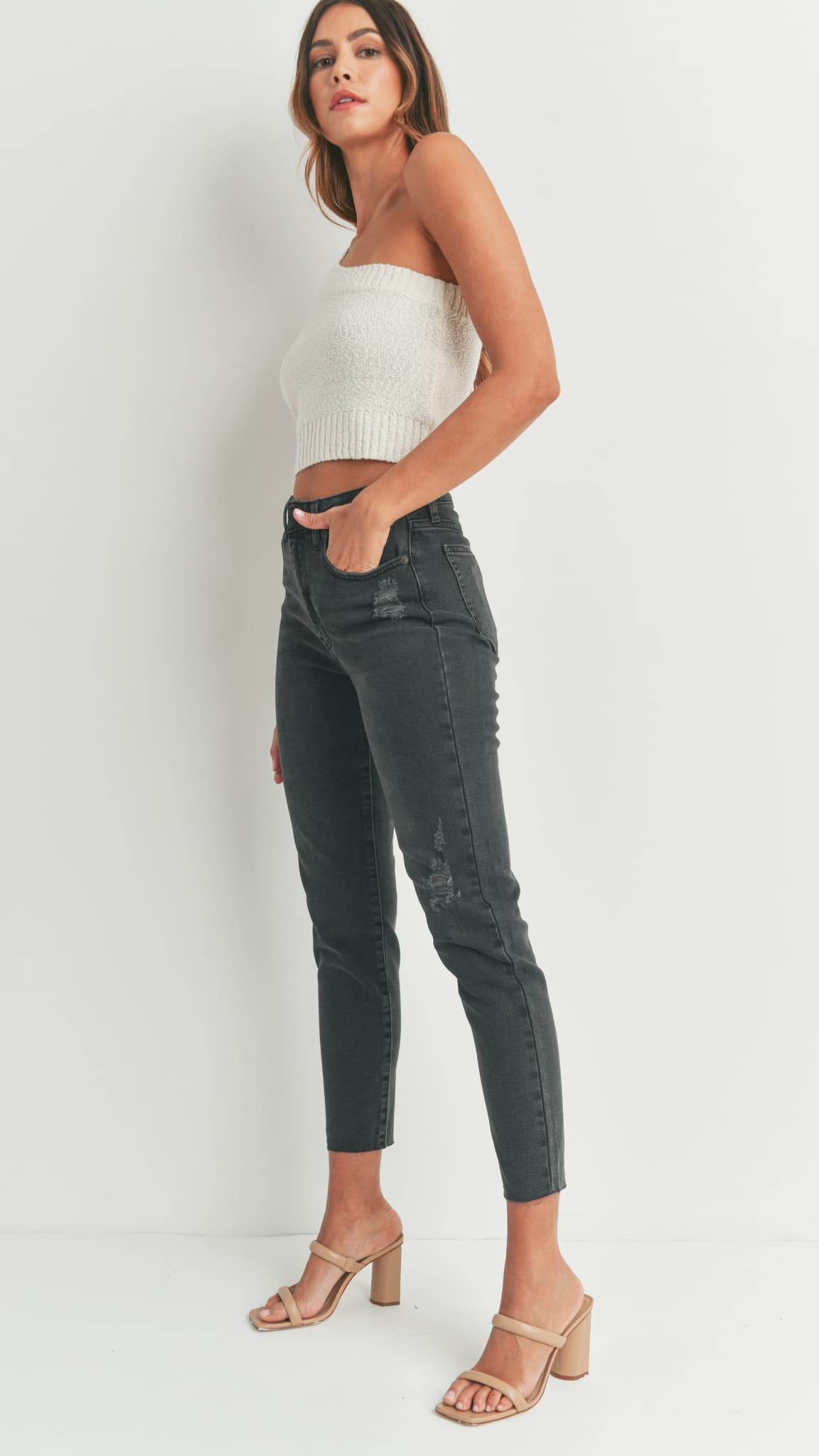 Woman in black skinny jeans, a white strapless knit top, and beige sandals