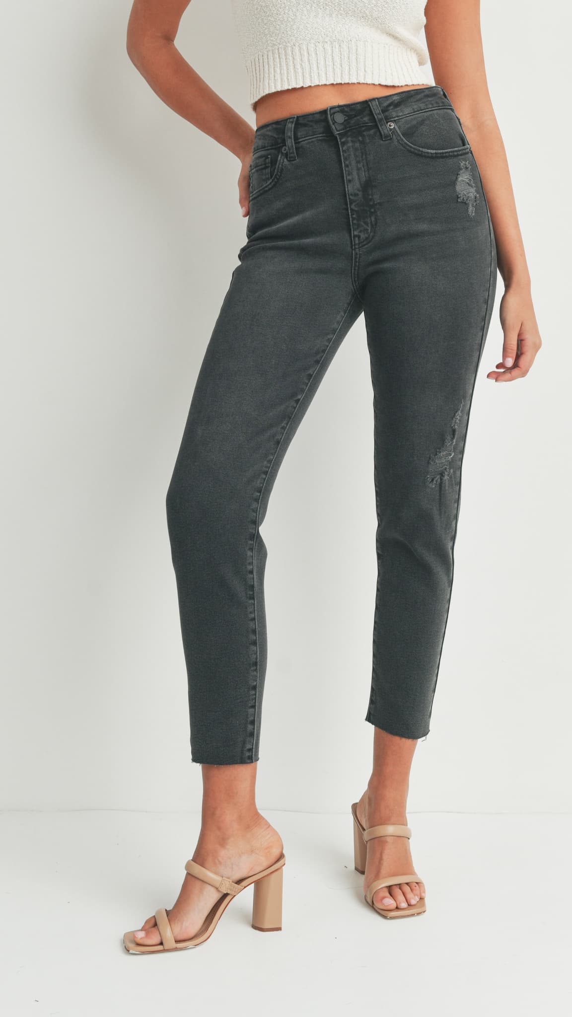 Close-up side view of black skinny jeans, white top, and beige heeled sandals