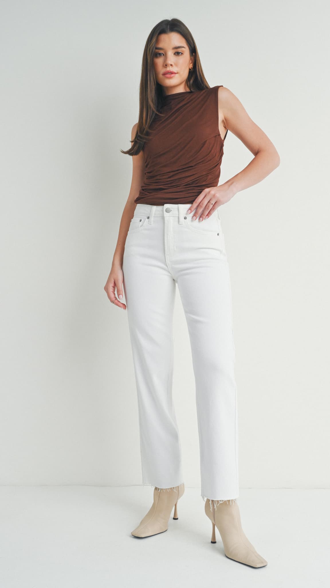 Woman in white straight-leg jeans, a brown sleeveless top, and beige heeled boots