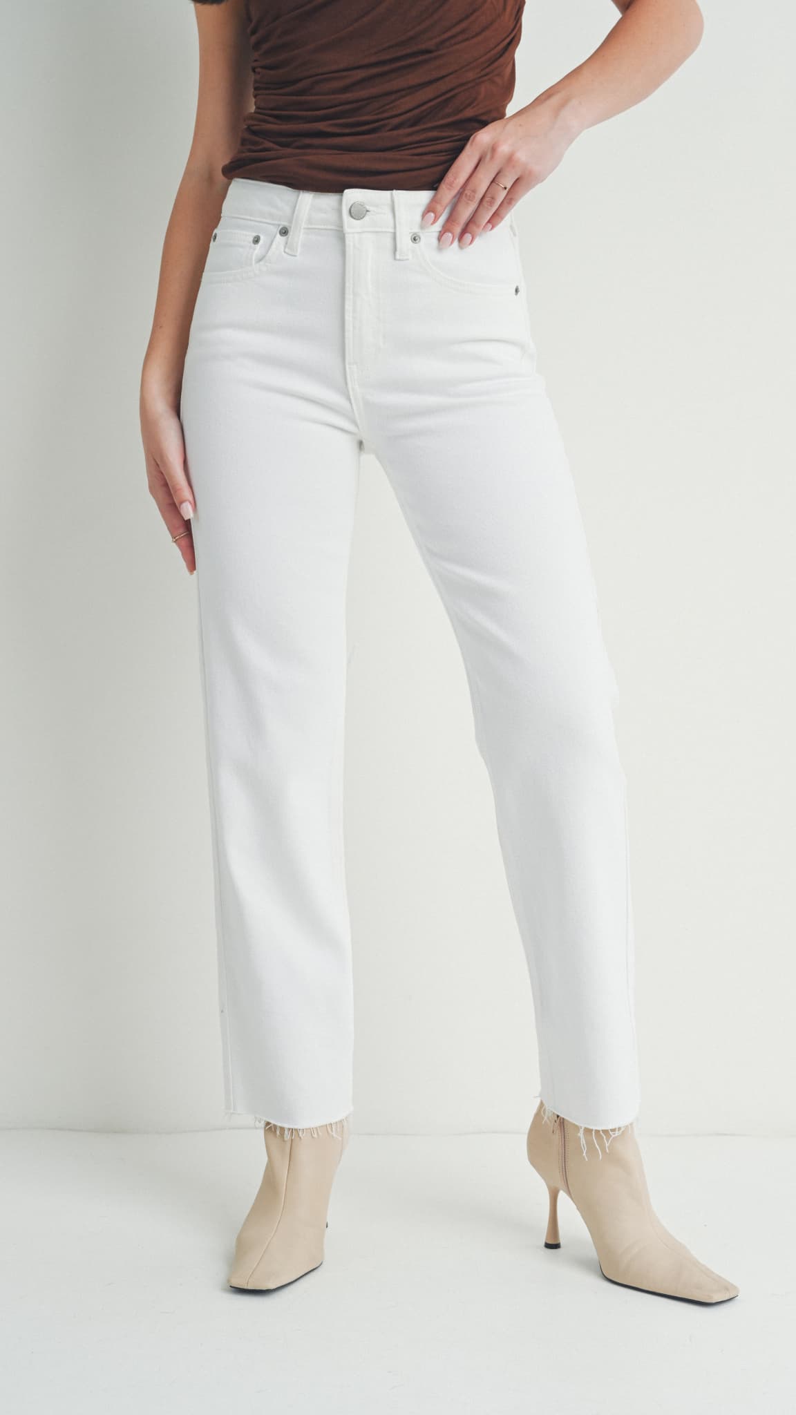 Close-up view of white straight-leg jeans, a brown sleeveless top and beige heeled boots