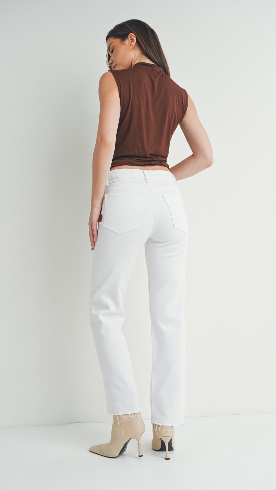 Back view of woman in white straight-leg jeans, a brown sleeveless top, and beige heeled boots