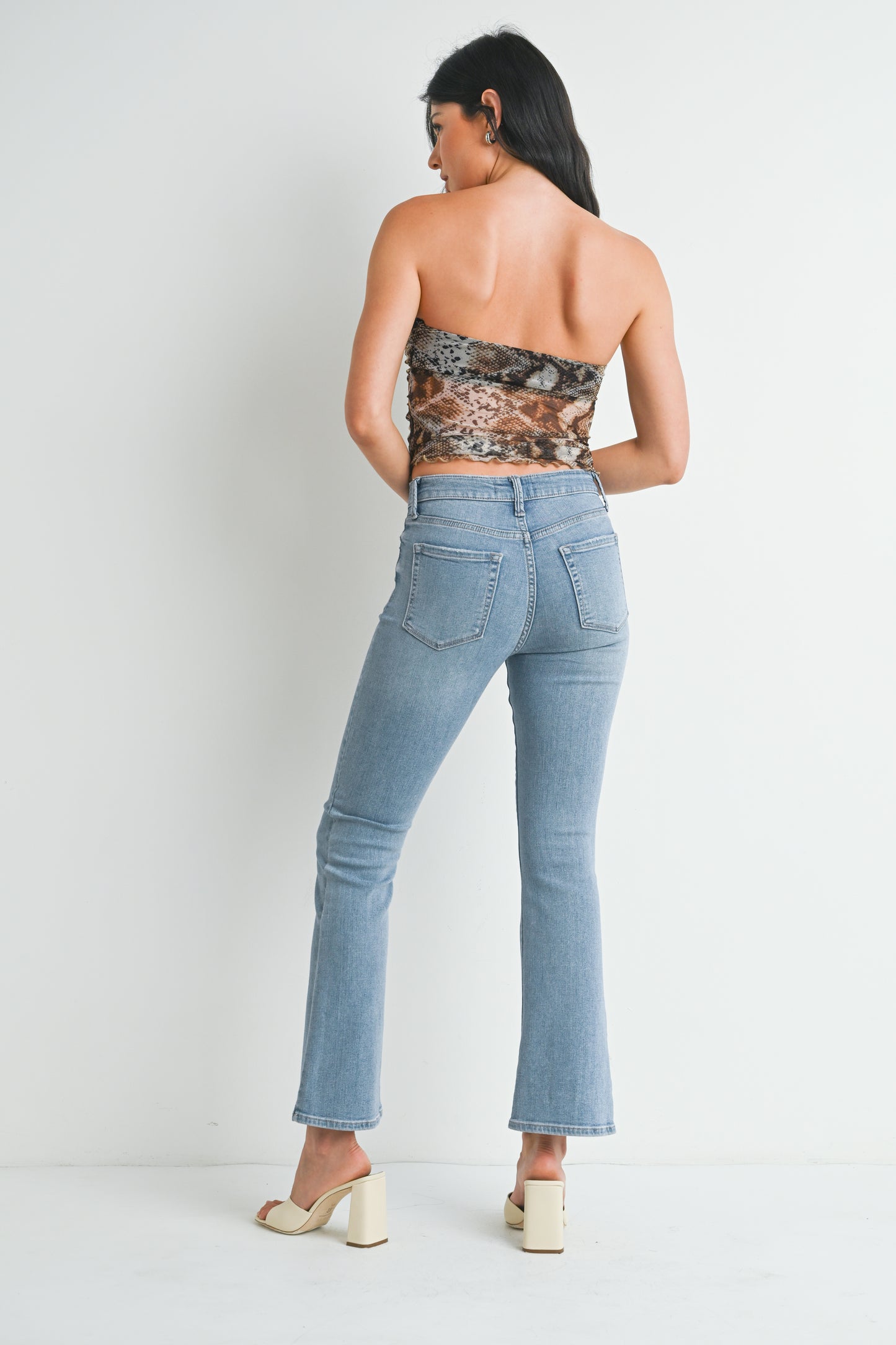 Woman wearing a strapless top with animal print and high-waisted jeans on a plain background