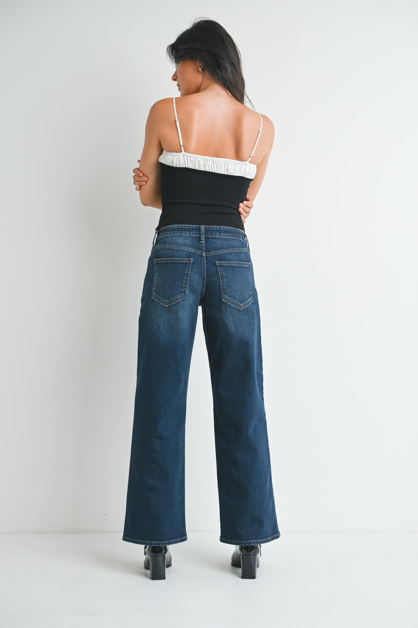 Woman wearing a black top and blue jeans against a white background