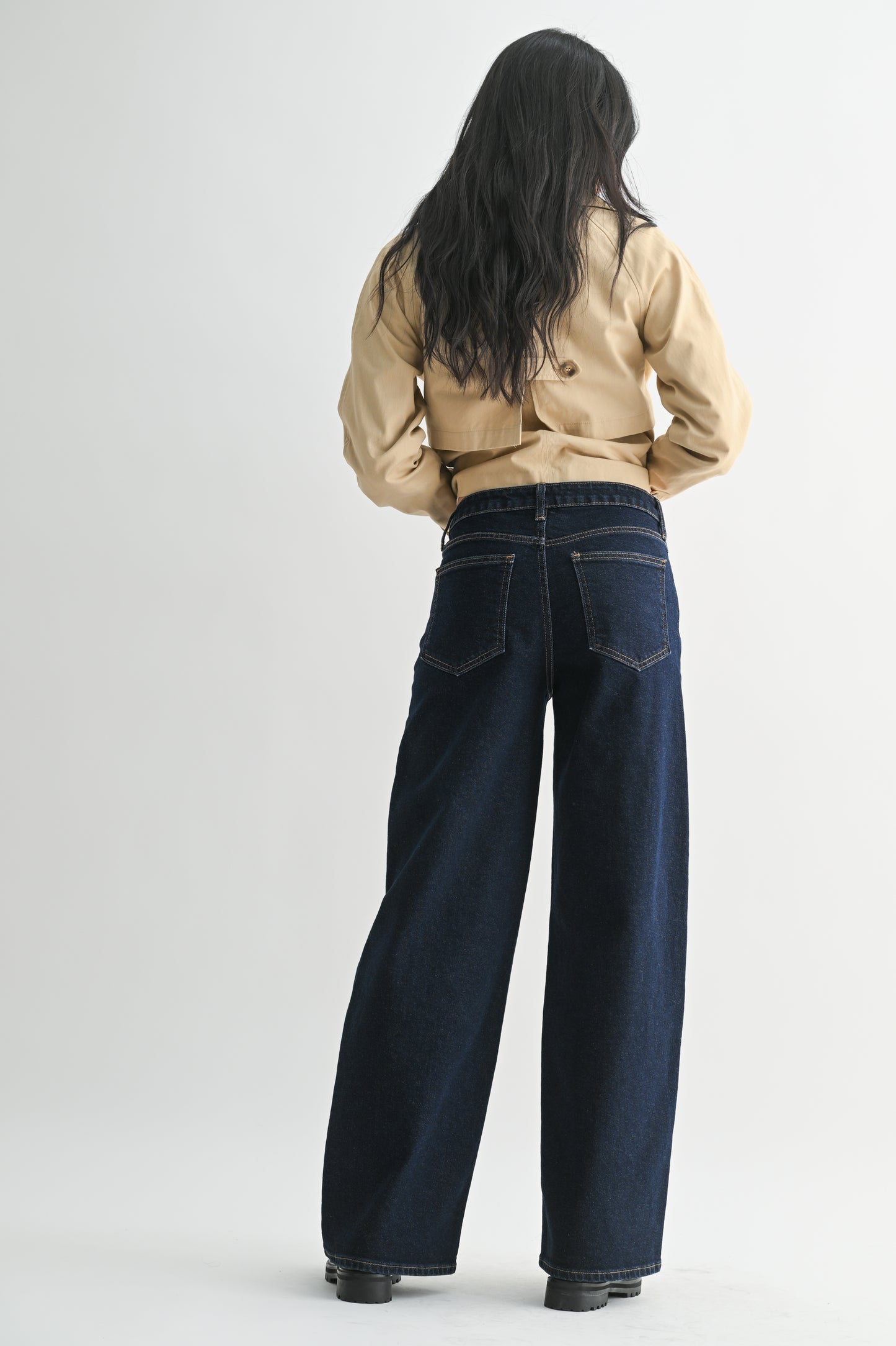 Person wearing a beige jacket and dark blue jeans on a white background