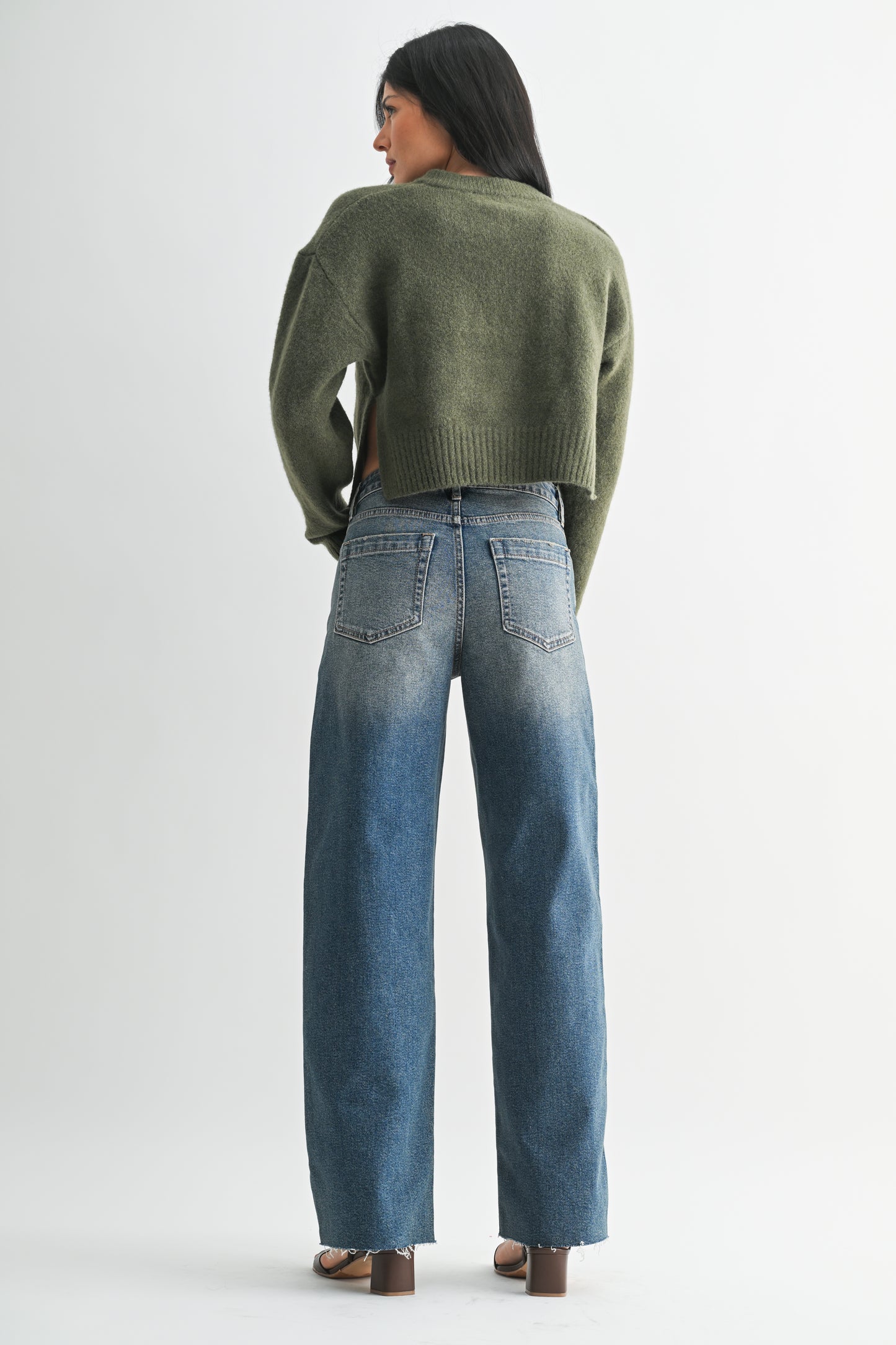 Person wearing a green sweater and blue jeans on a white background