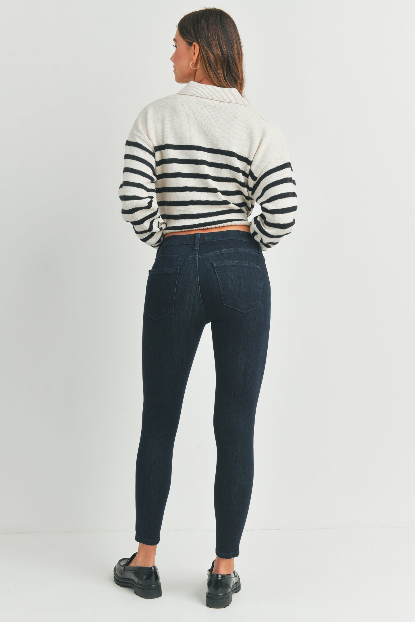 Woman wearing a striped sweater and dark jeans on a white background