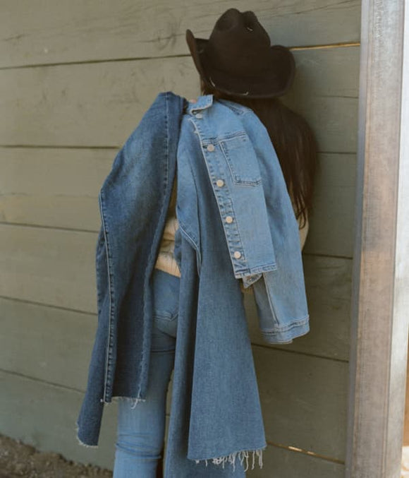 Woman against a wall facing backwards with a demin clothing slung over the shoulder