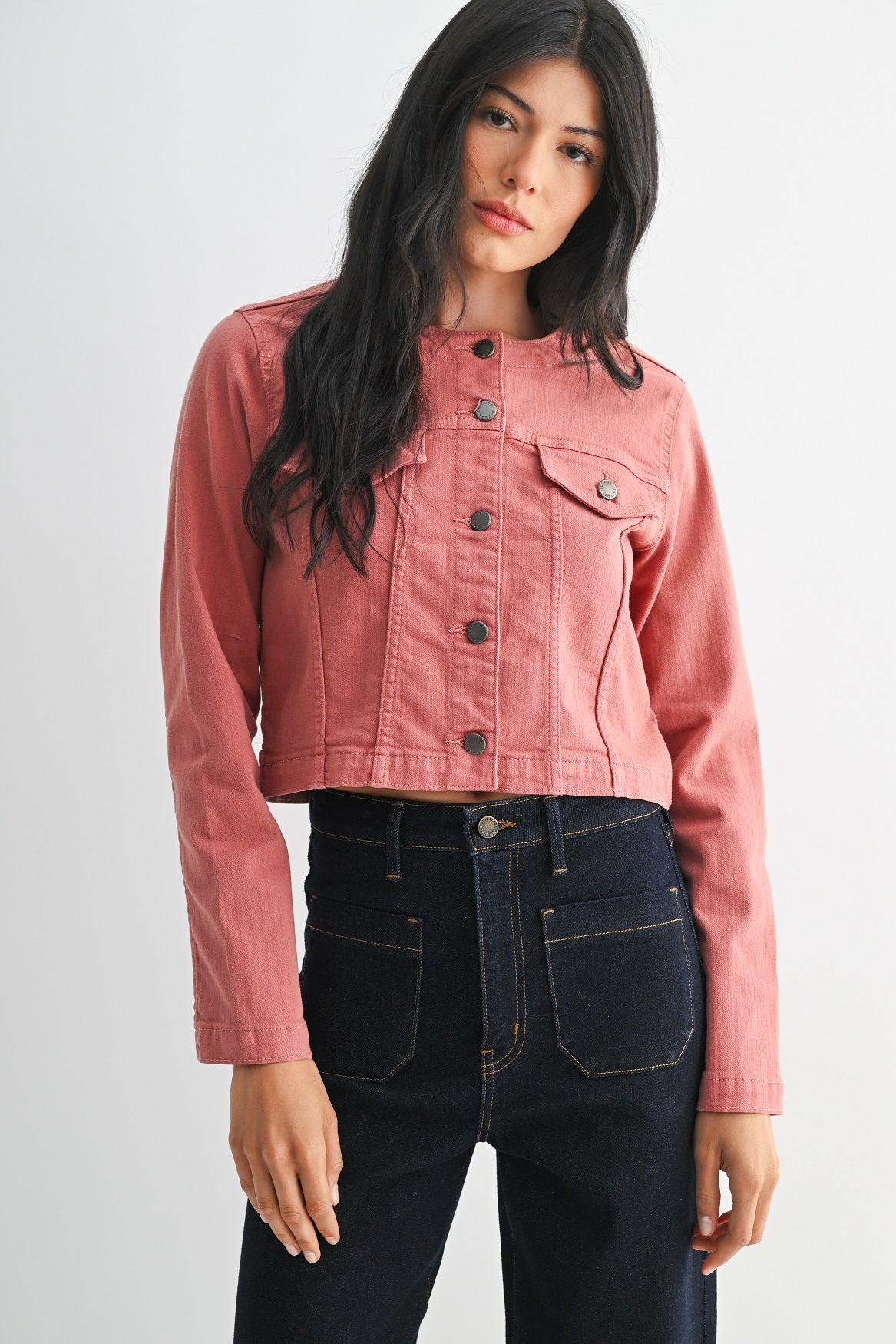 Woman wearing a pink denim jacket and black jeans on a white background