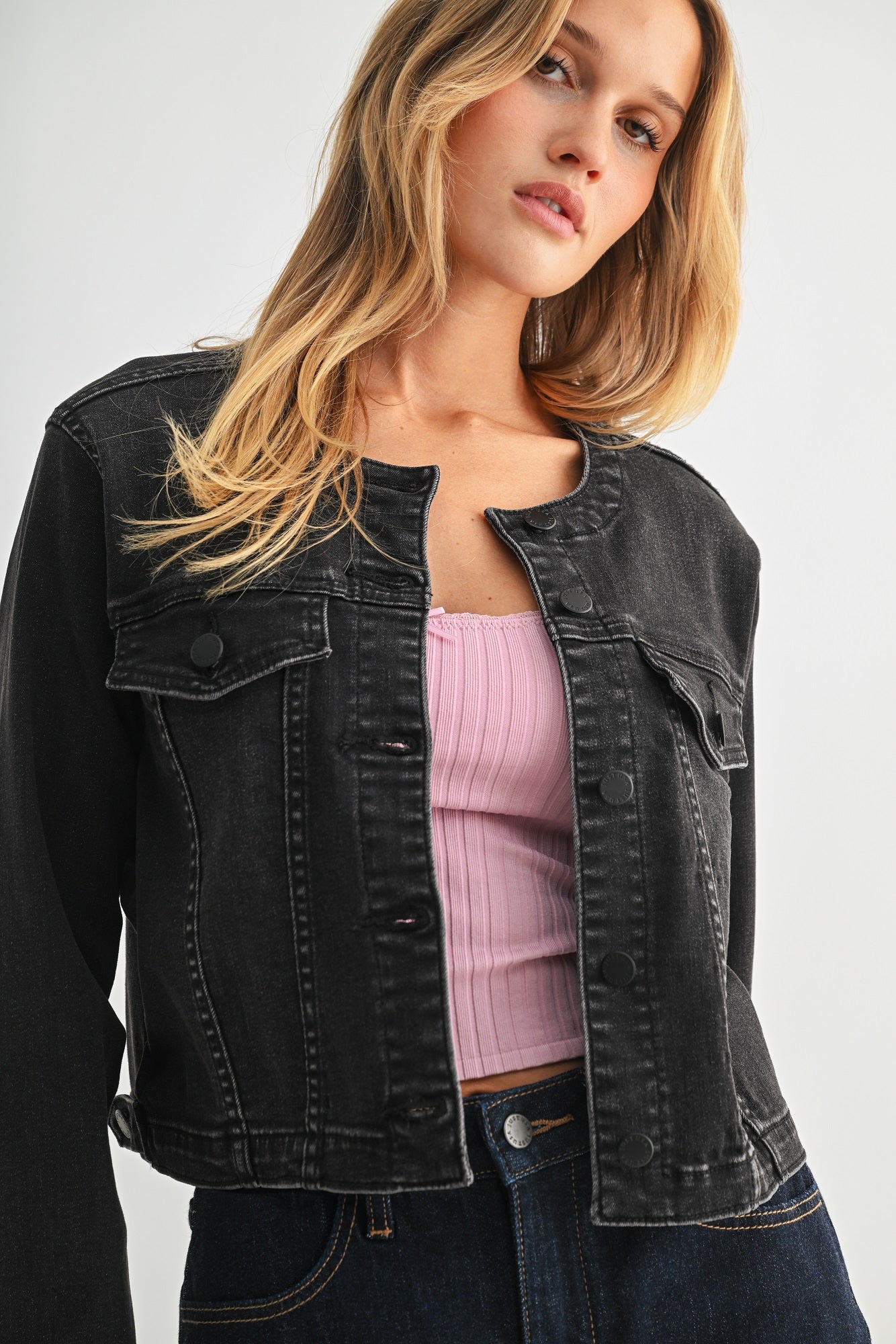 Woman wearing a black denim jacket over a pink top on a white background