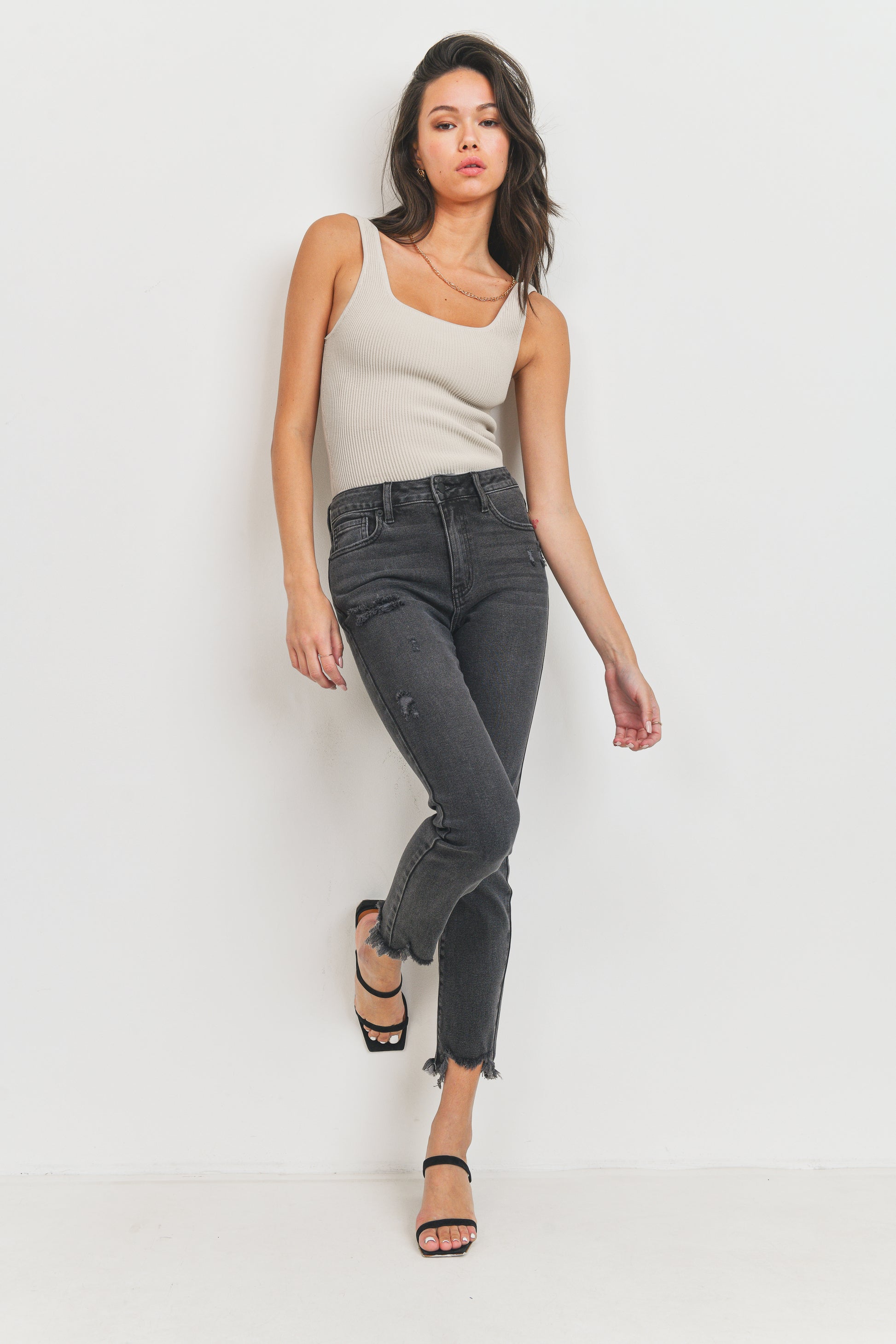 Woman wearing a beige tank top and black jeans on a white background