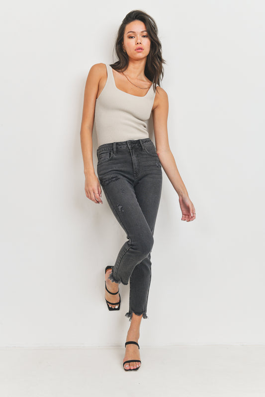 Woman wearing a beige tank top and black jeans on a white background