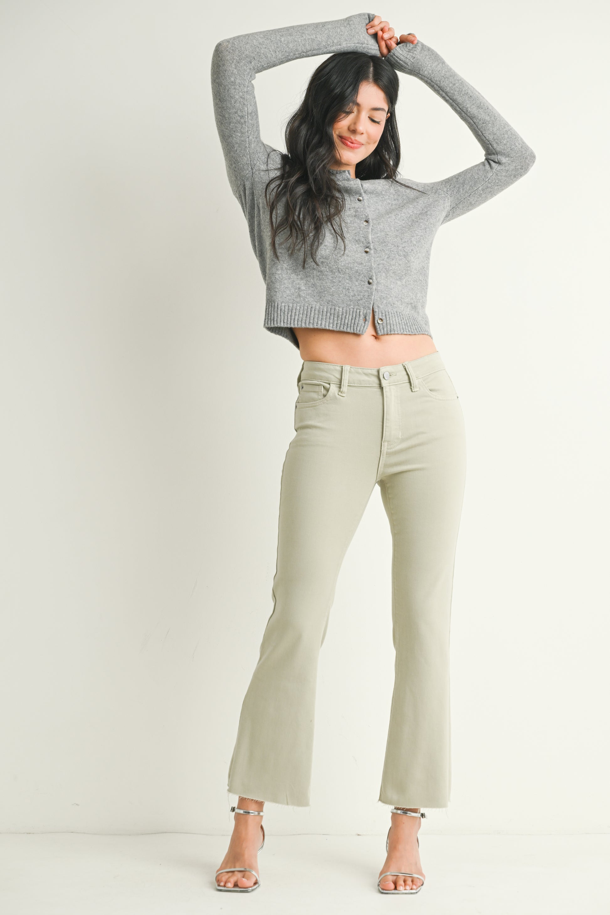 Woman wearing a gray cropped sweater and light green pants on a white background