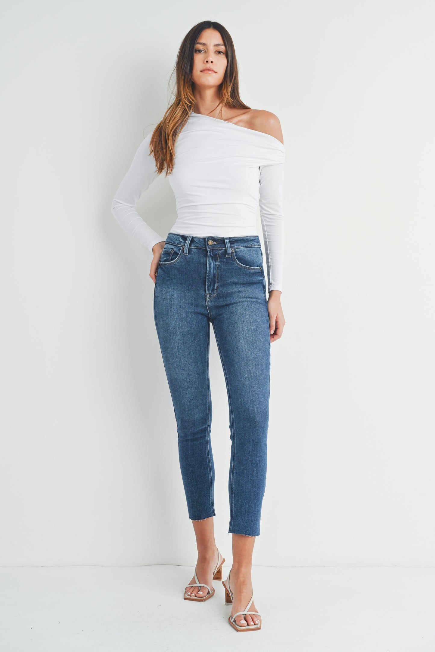 Woman wearing a white off-shoulder top and blue jeans against a white background