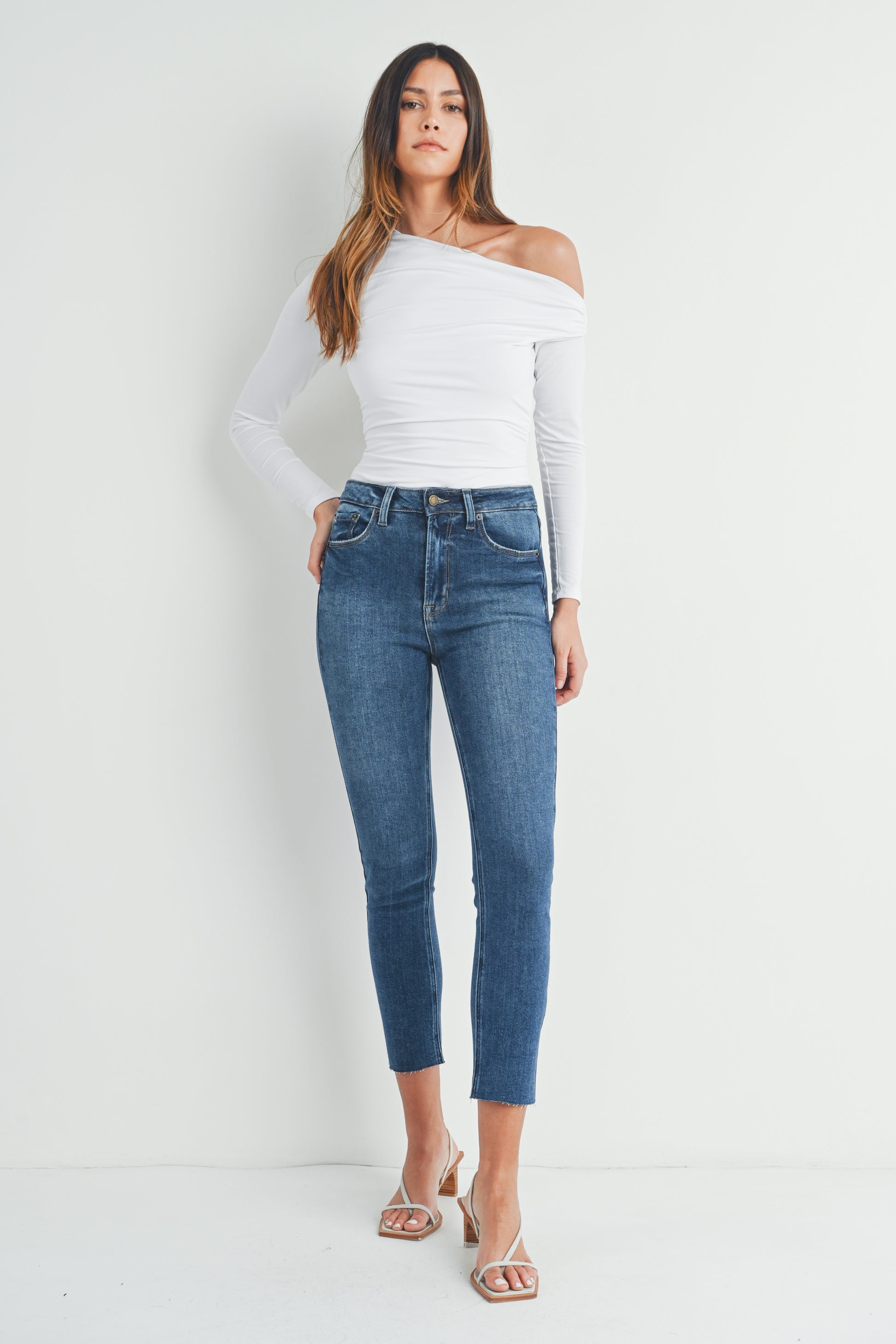 Woman wearing a white off-shoulder top and blue jeans against a white background