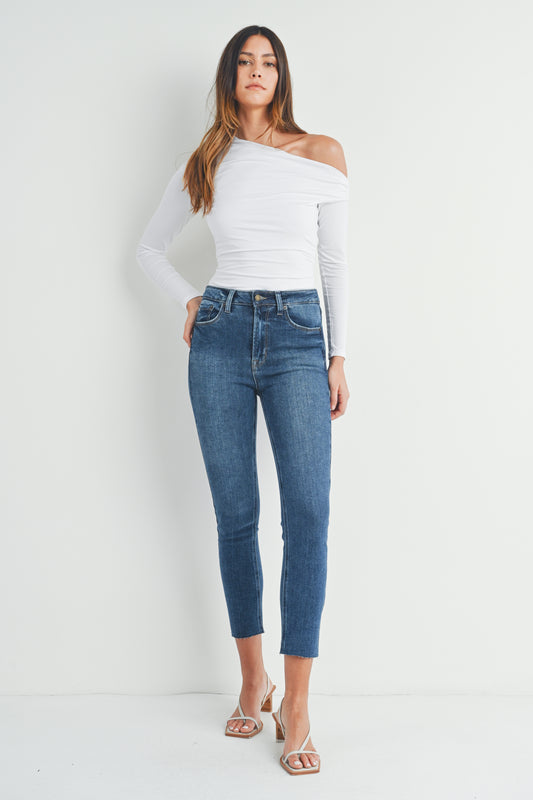 Woman wearing a white off-shoulder top and blue jeans against a white background