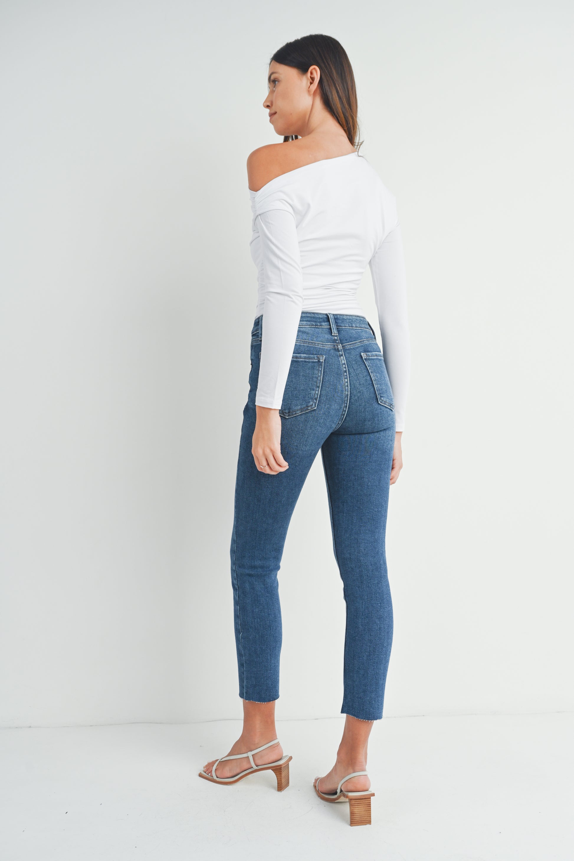 Woman wearing a white off-shoulder top and blue jeans on a white background