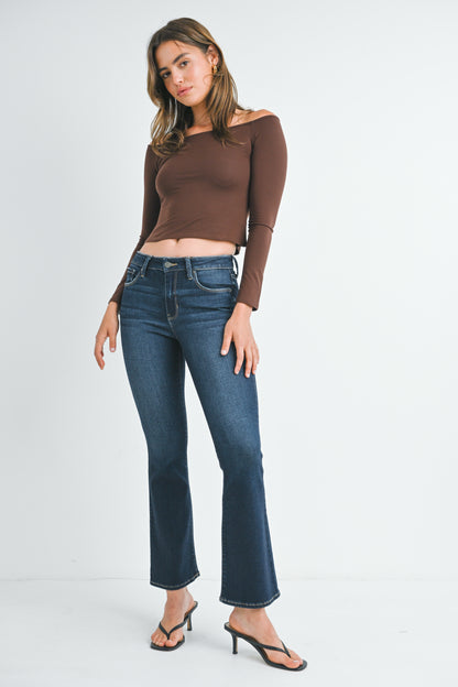 Woman wearing a brown off-shoulder top and blue jeans on a white background