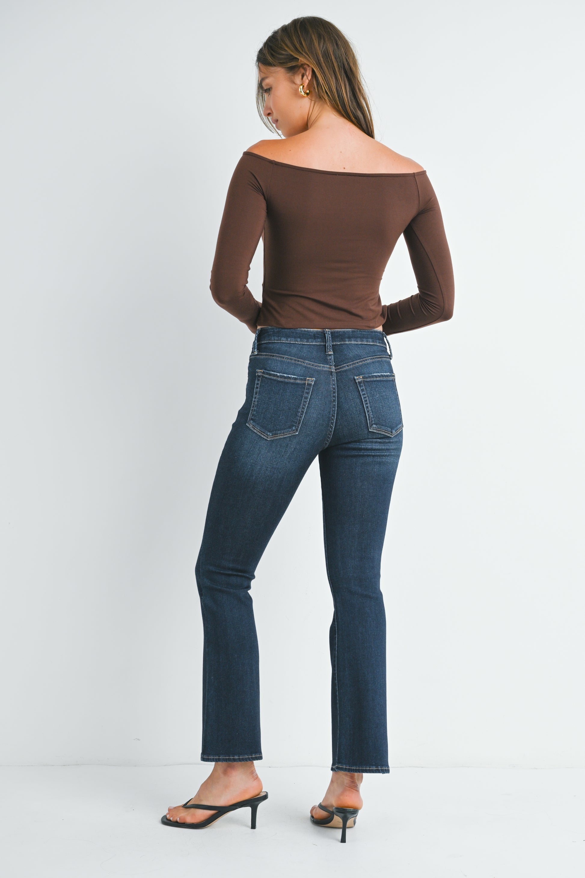 Woman wearing blue jeans and a brown top on a white background