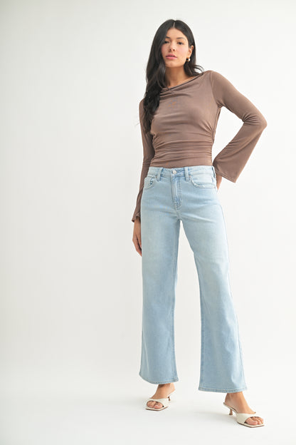 Woman wearing a brown long-sleeve top and light blue jeans on a white background