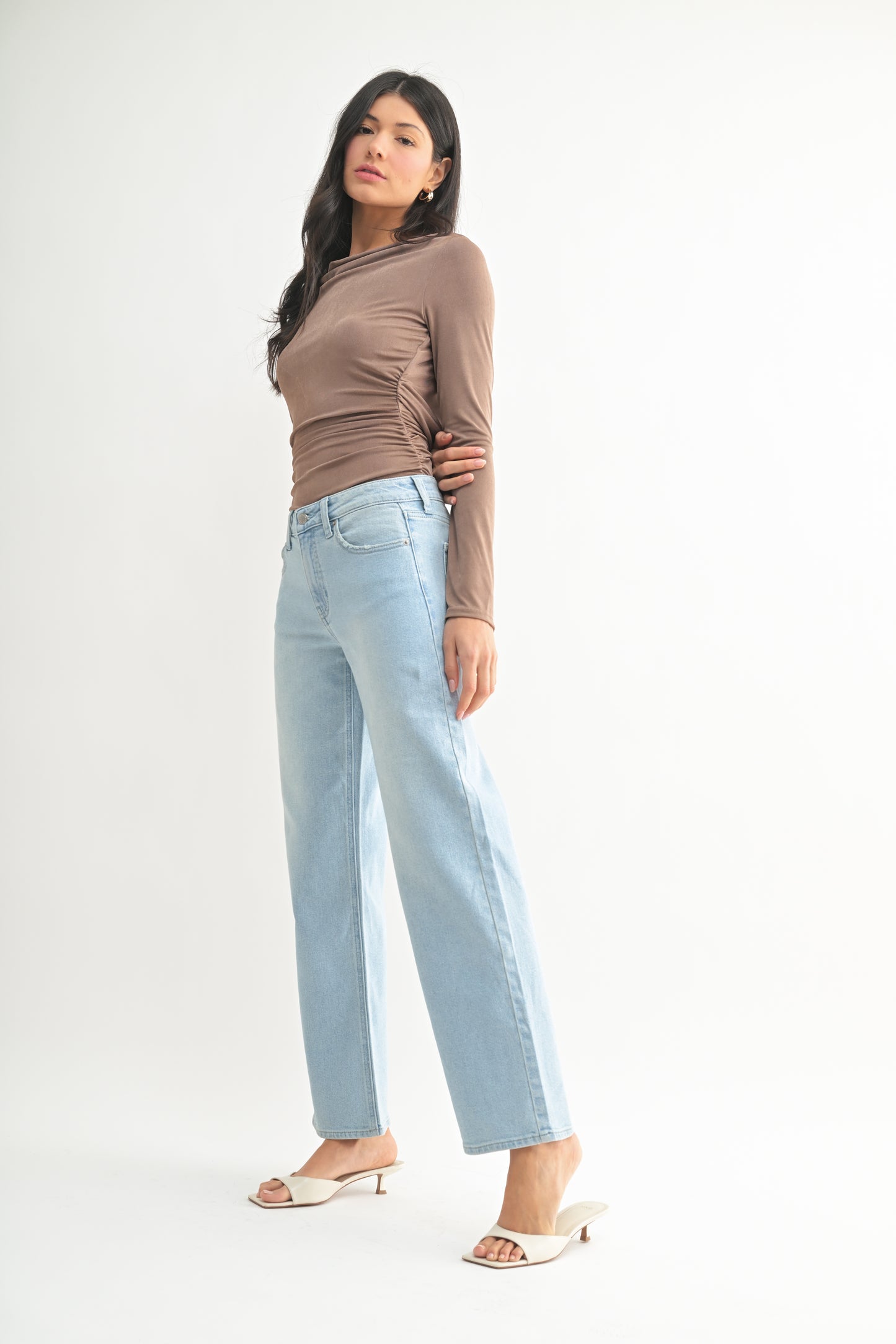 Woman wearing a brown top and light blue jeans on a white background