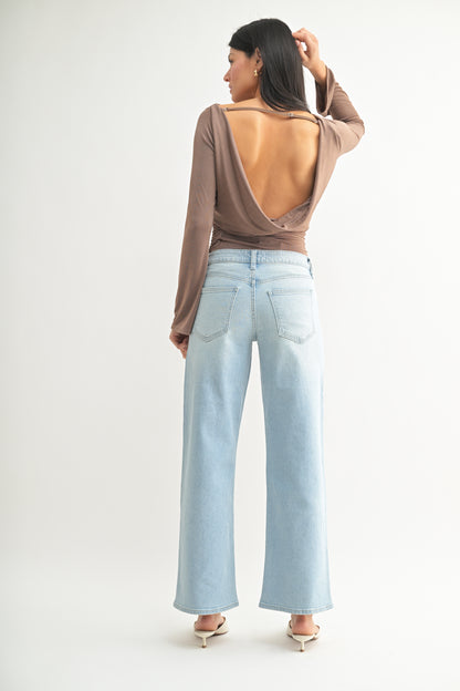 Woman wearing a brown open-back top and light blue jeans on a white background