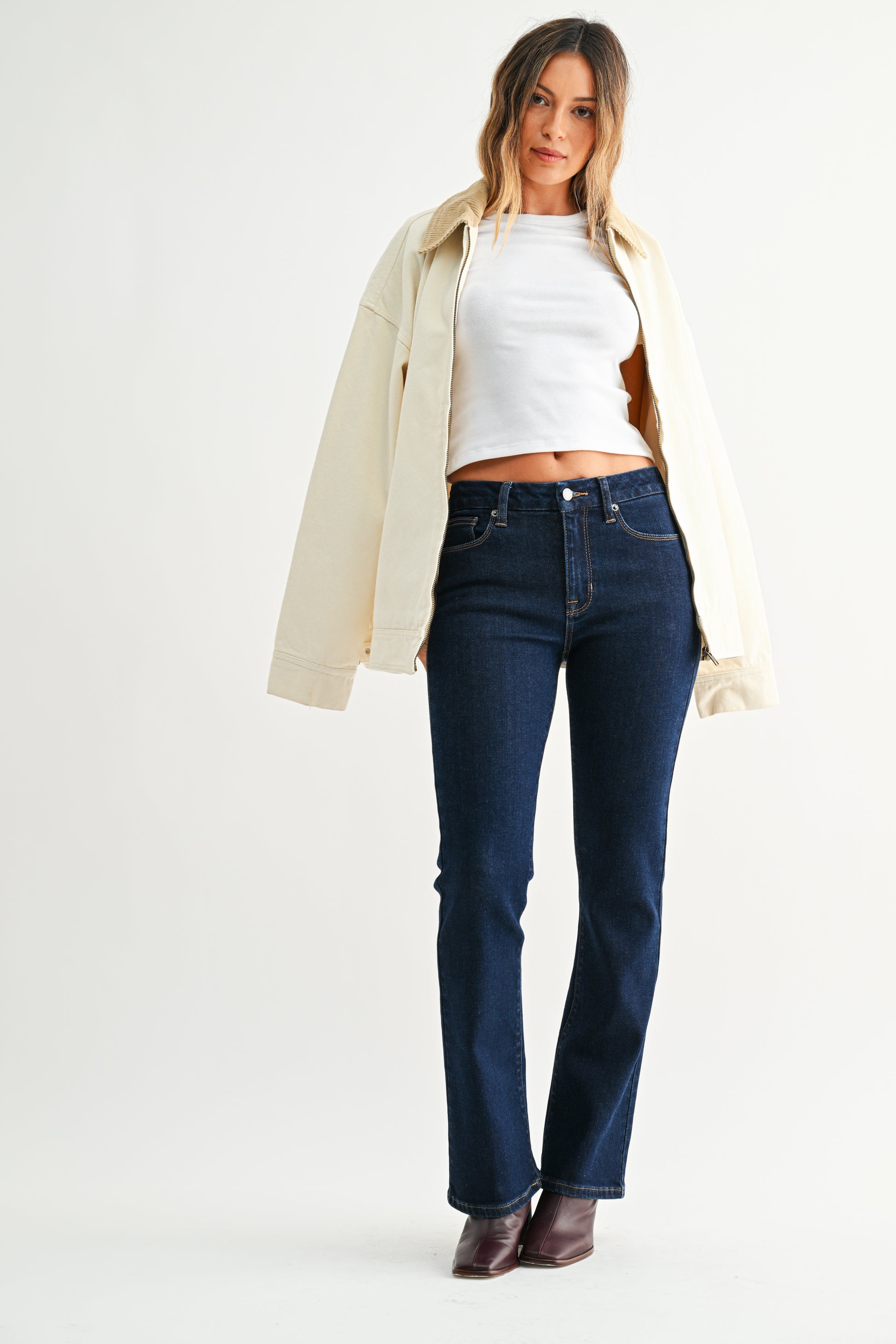 Woman wearing a white shirt, beige jacket, and dark blue jeans on a white background