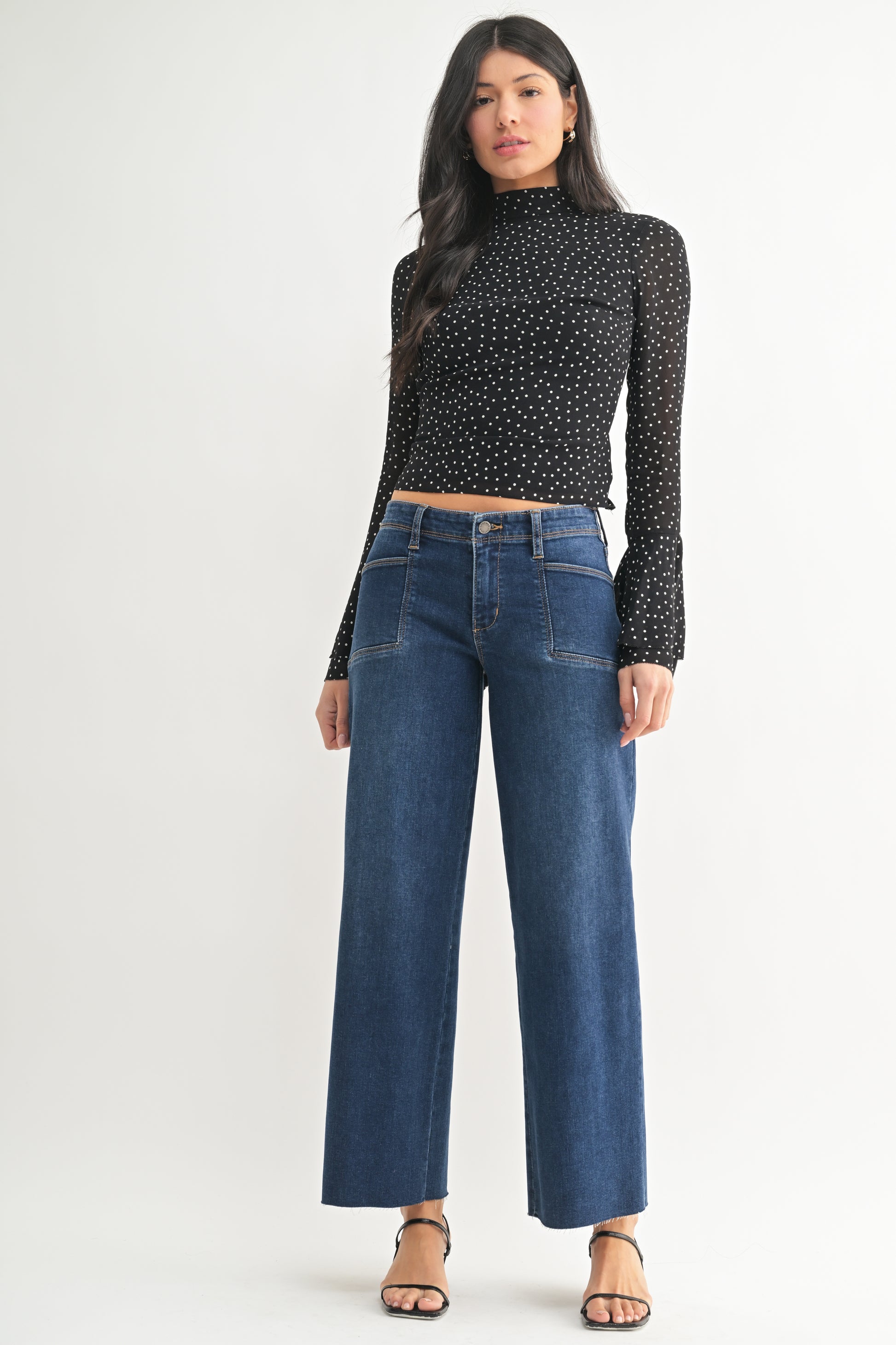 Woman wearing a black polka dot top and blue jeans on a white background