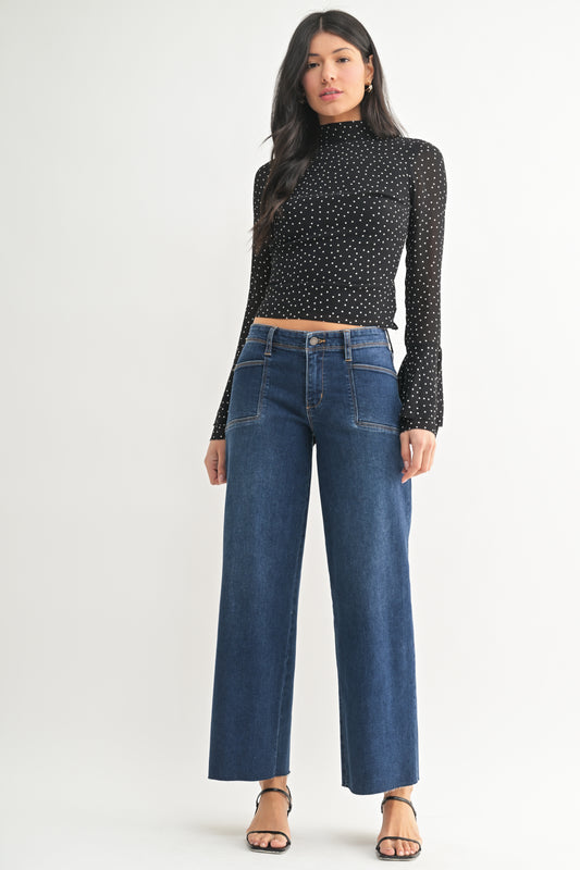 Woman wearing a black polka dot top and blue jeans on a white background