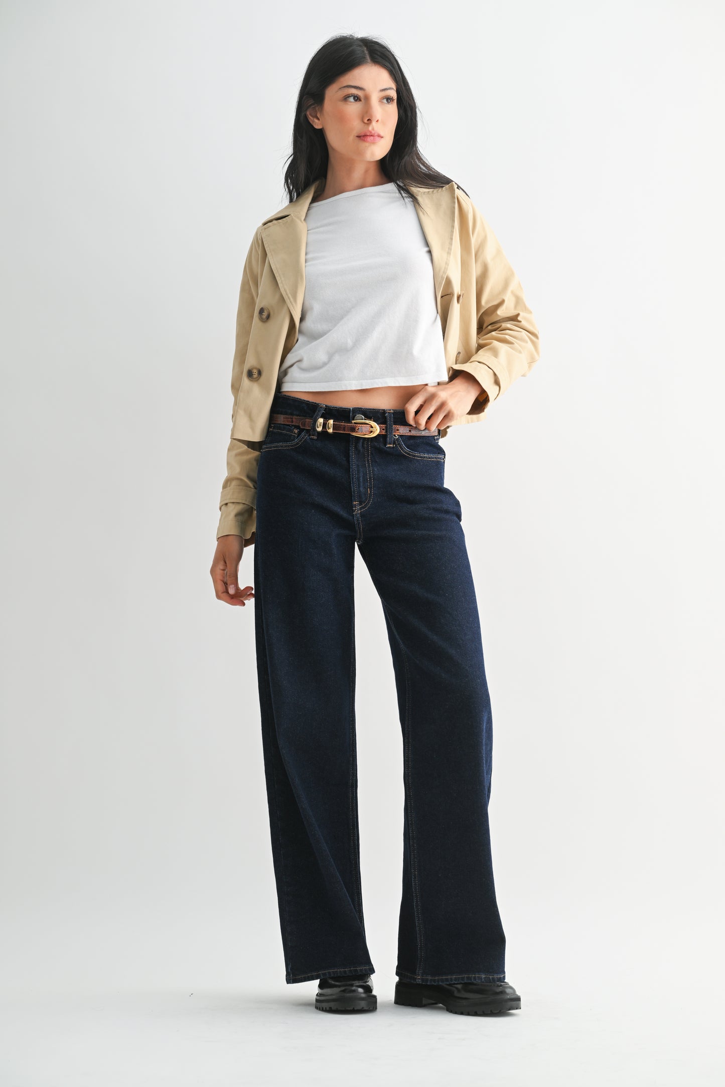 Woman wearing a beige jacket, white shirt, and dark jeans on a white background