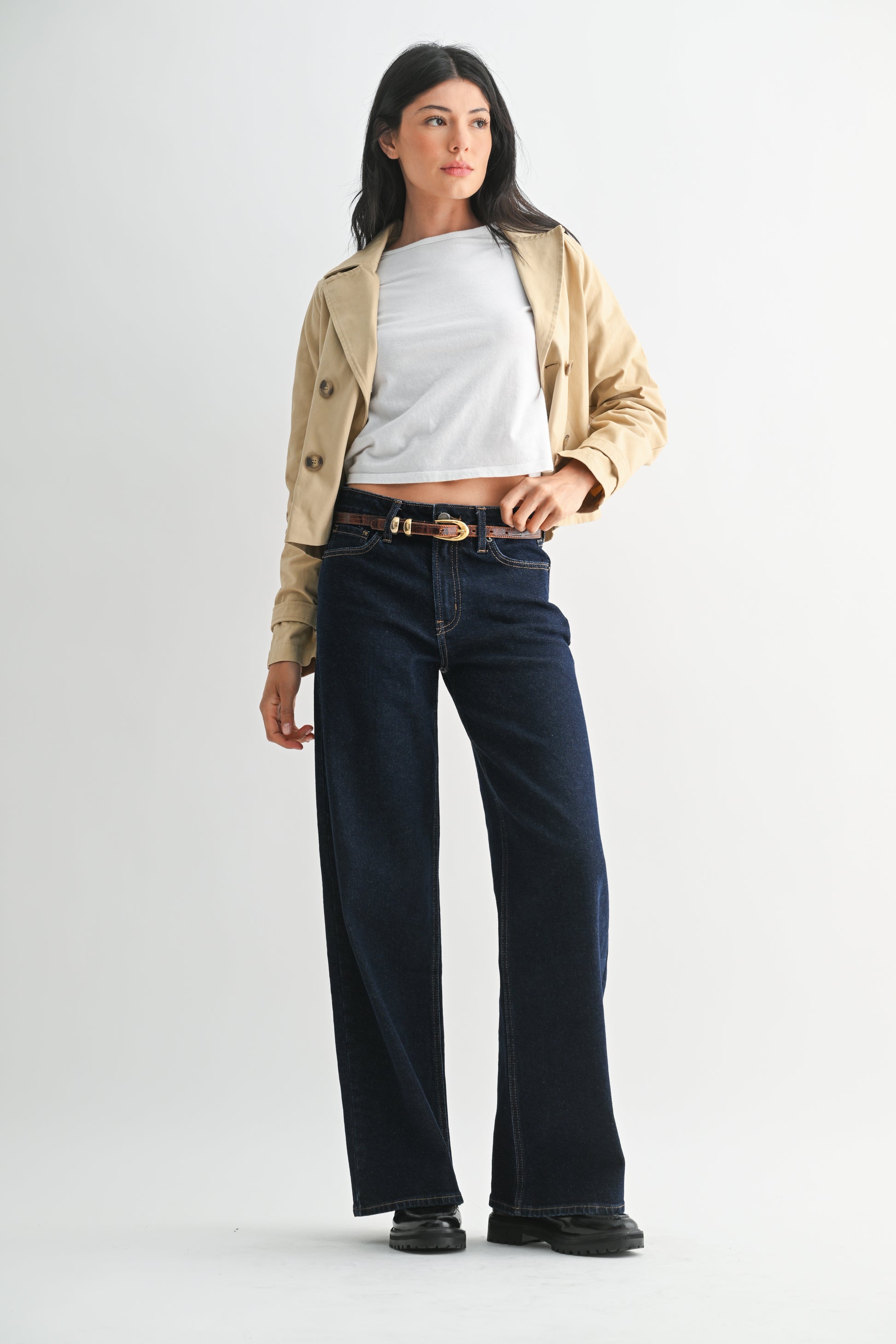 Woman wearing a beige jacket, white shirt, and dark jeans on a white background