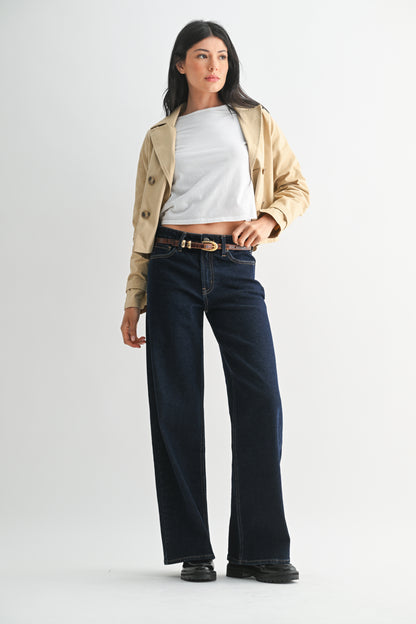 Woman wearing a beige jacket, white shirt, and dark jeans on a white background
