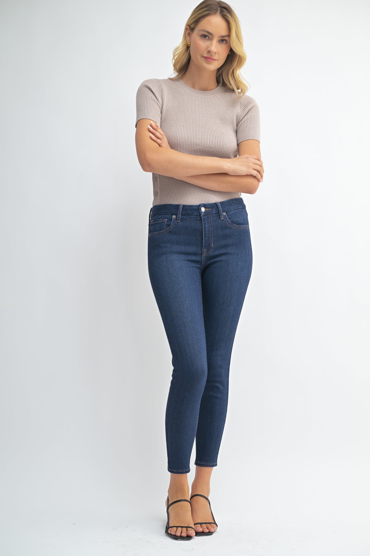 Woman wearing a beige top and blue jeans on a white background