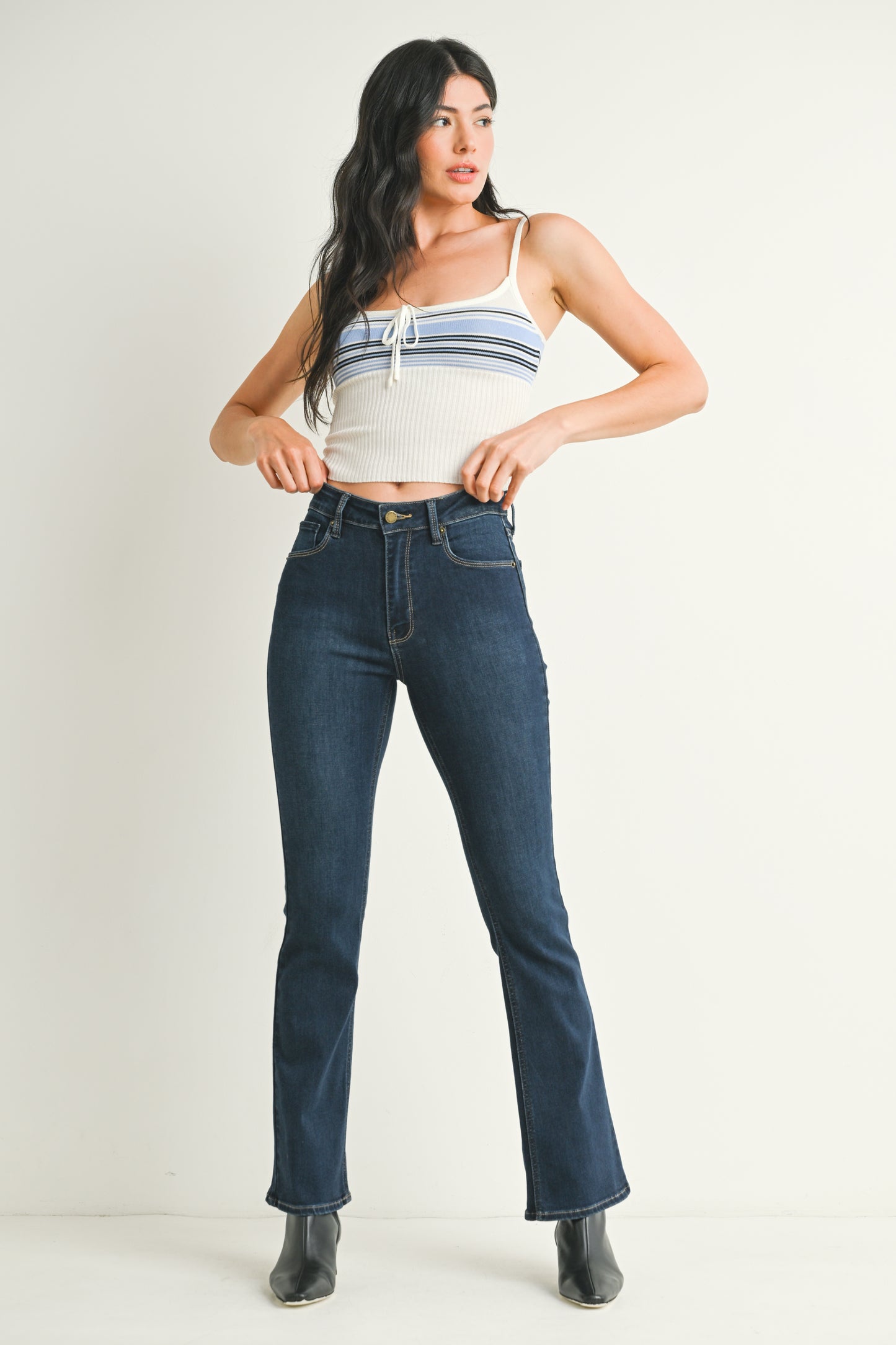 Woman wearing a white crop top with blue stripes and dark blue jeans on a plain background