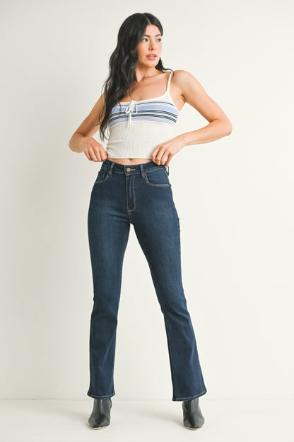 Woman wearing a white crop top with blue stripes and dark blue jeans on a plain background