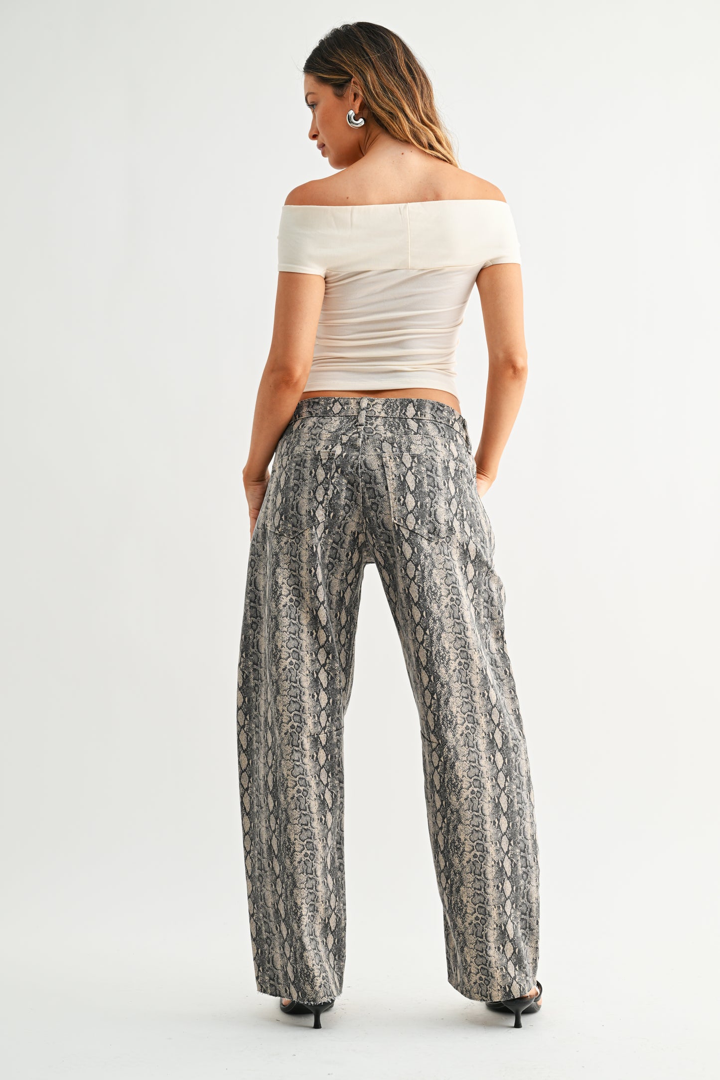 Woman wearing a white off-shoulder top and patterned pants on a white background
