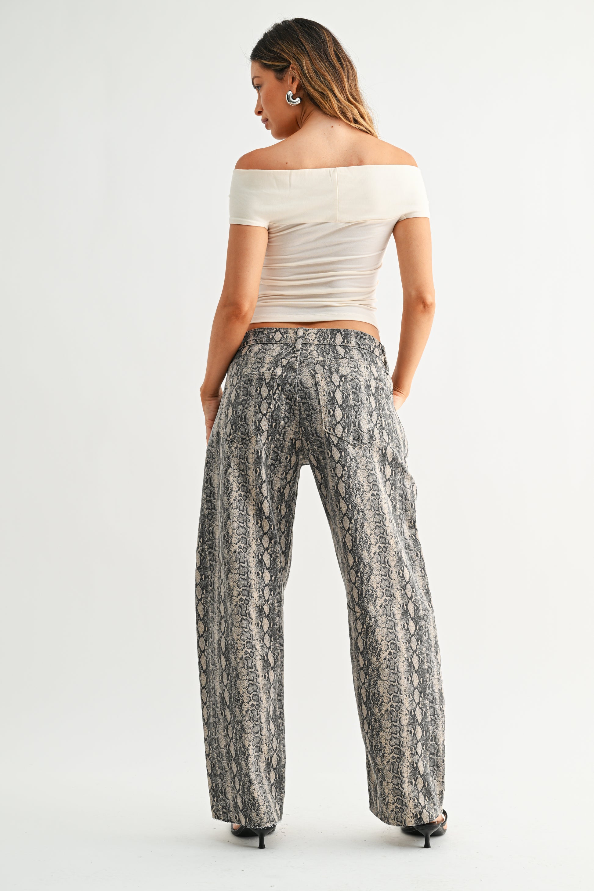 Woman wearing a white off-shoulder top and patterned pants on a white background