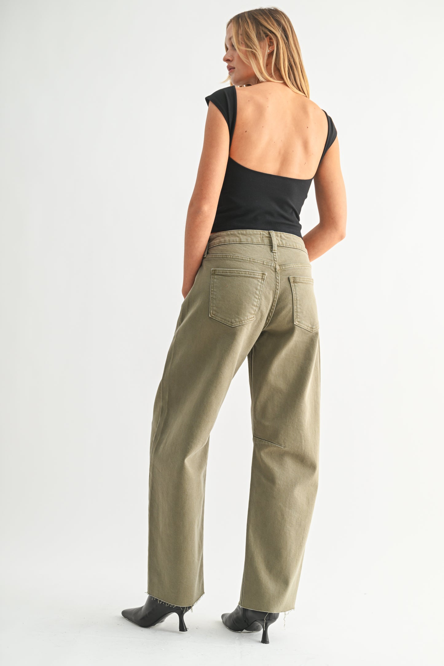 Woman wearing beige pants and a black top on a white background