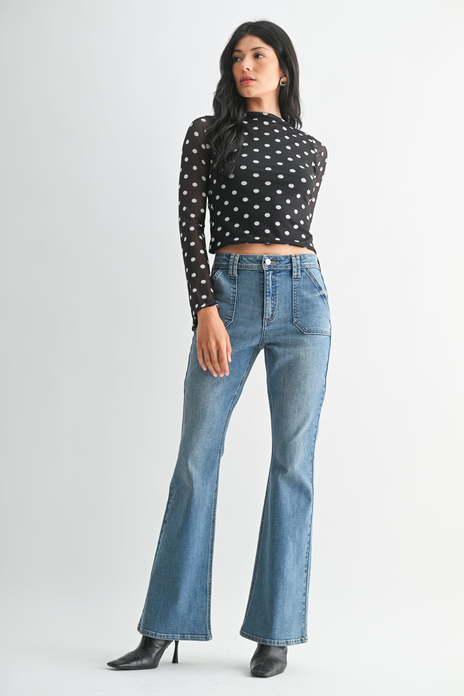 Woman wearing a black polka dot top and blue jeans on a white background