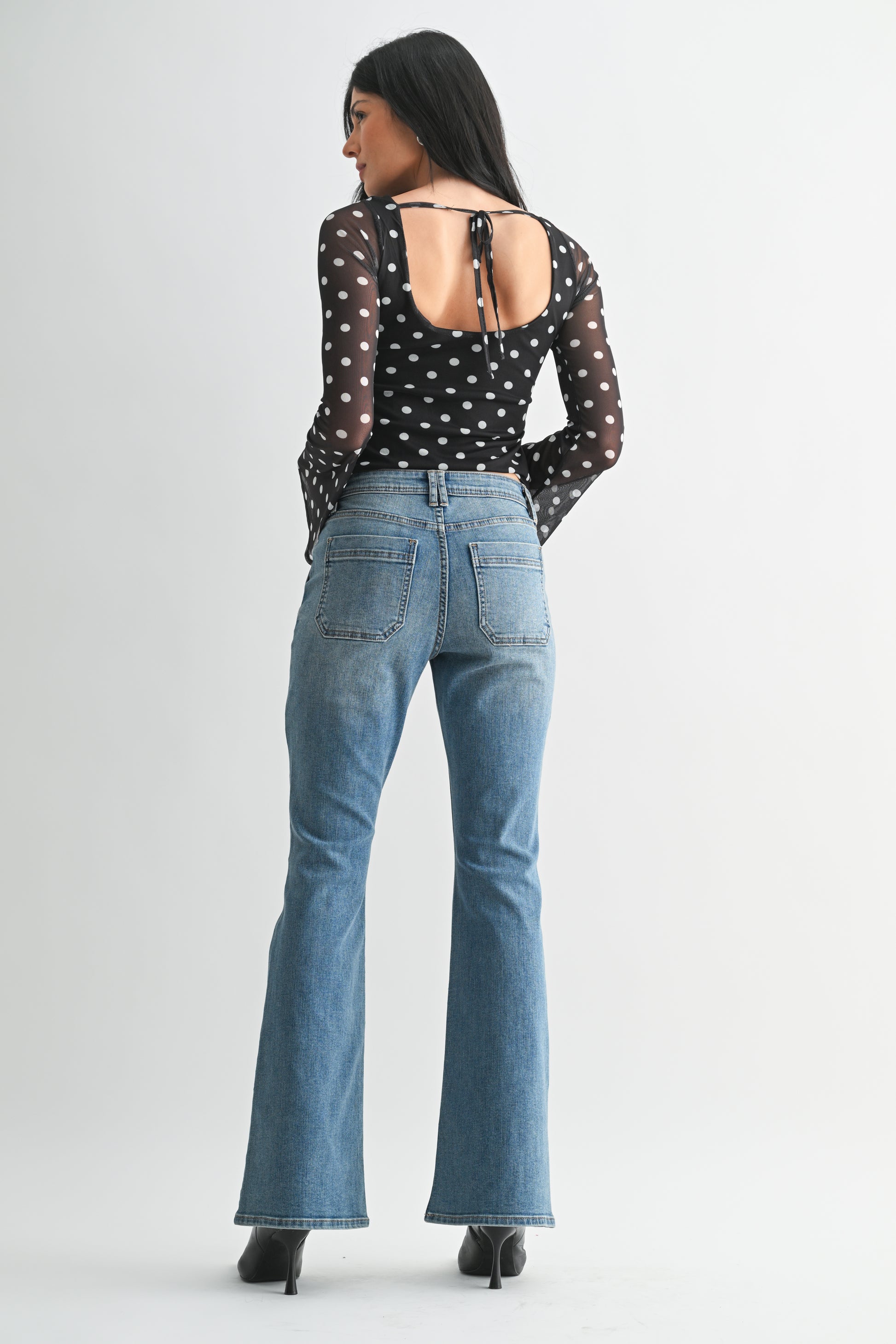 Woman wearing a black polka dot top and blue jeans on a white background