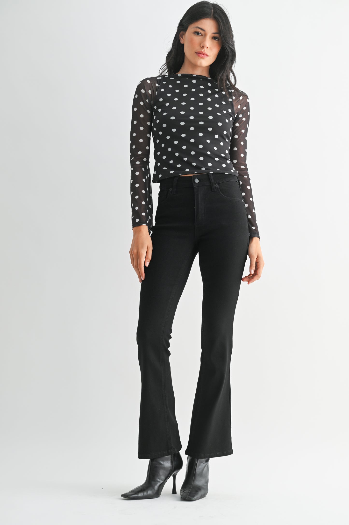 Woman wearing a black polka dot top and black pants on a white background