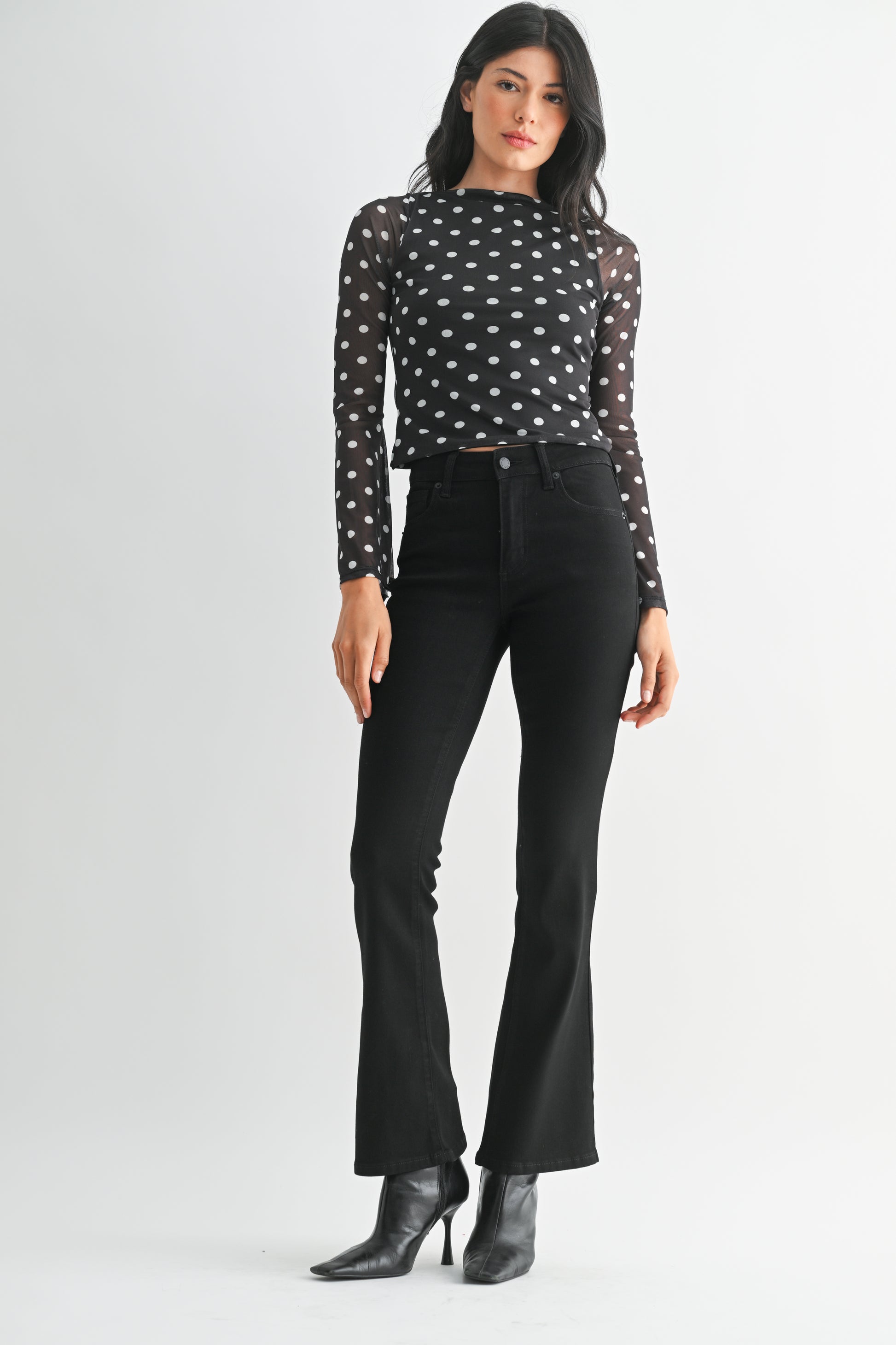 Woman wearing a black polka dot top and black pants on a white background