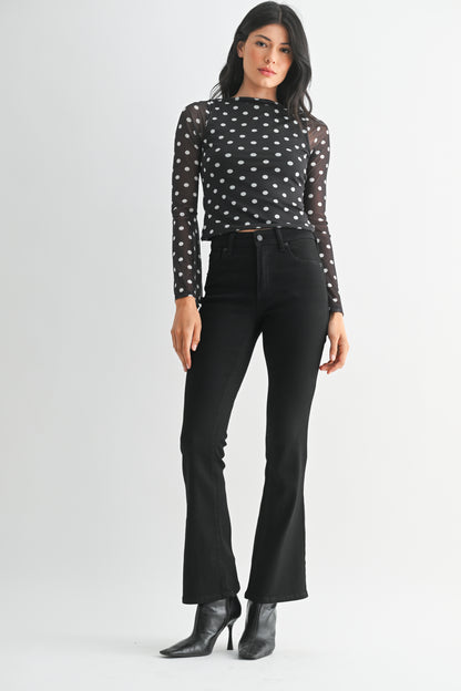 Woman wearing a black polka dot top and black pants on a white background