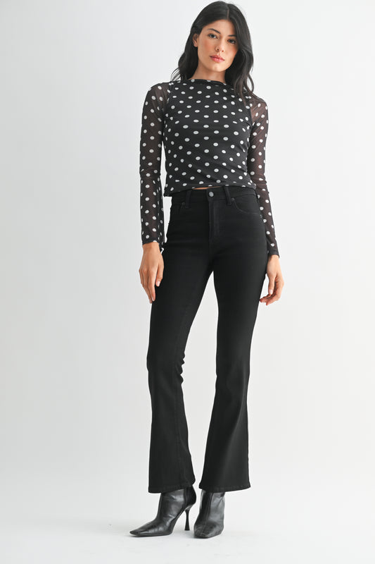 Woman wearing a black polka dot top and black pants on a white background