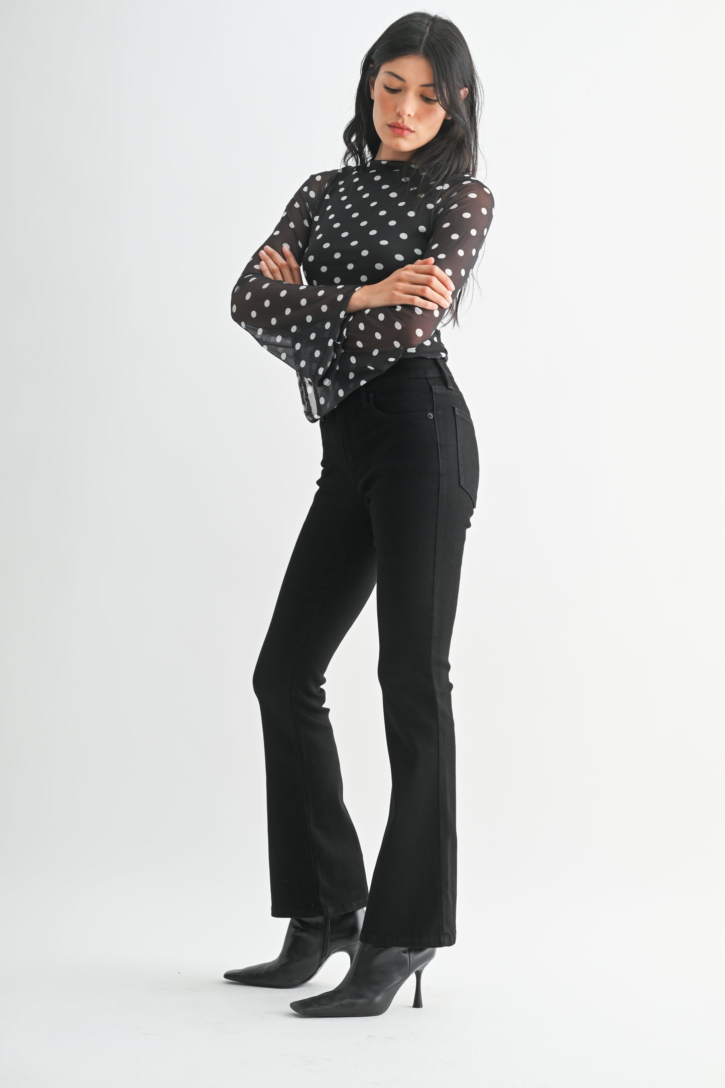 Woman wearing a black polka dot blouse and black pants on a white background