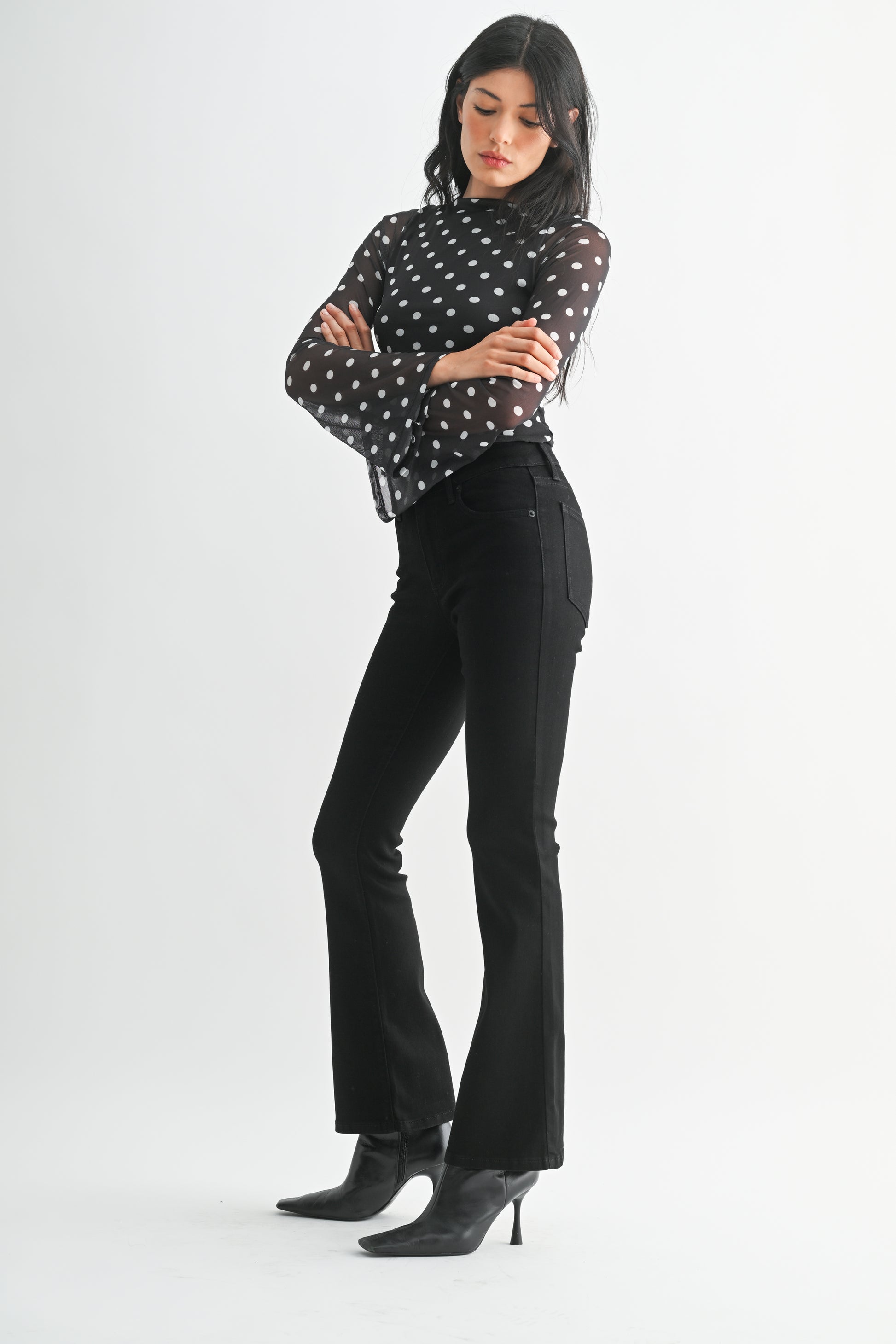 Woman wearing a black polka dot blouse and black pants on a white background