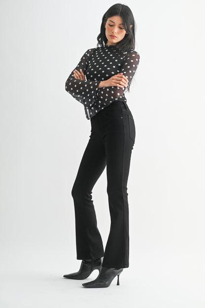 Woman wearing a black polka dot blouse and black pants on a white background